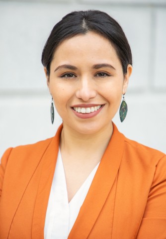 Chantiri Abarcaz smiling in an orange top and leaf-shaped earrings against a neutral background.