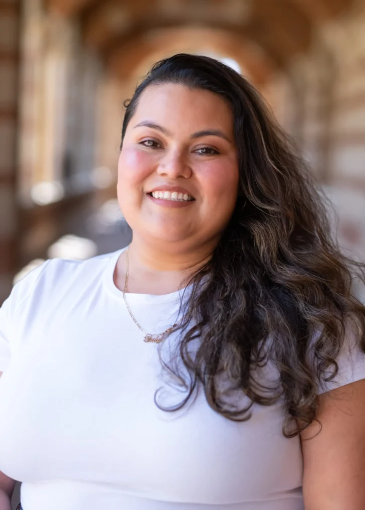 Gabriela Dominguez smiling in a white top and with long dark hair, with Royce Hall softly blurred behind her.