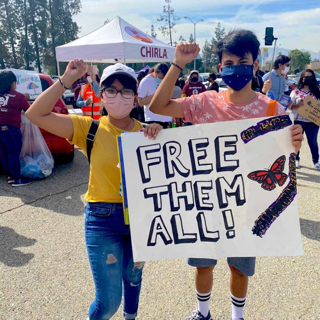 Two youth holding up a "Free Them All" sign