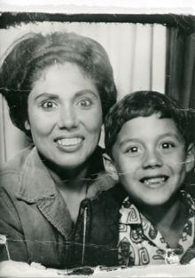 Black and white historical photo of a woman smiling and a young boy posing together with their faces close to each other.