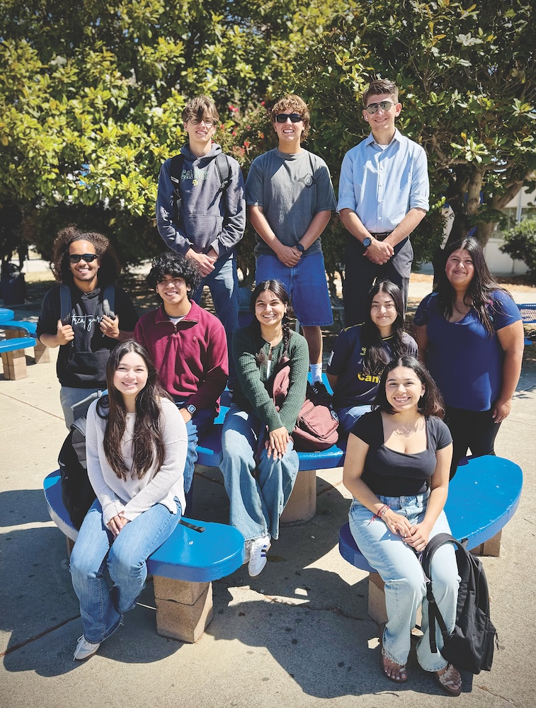 A group of about ten students posing together outdoors around blue chairs.