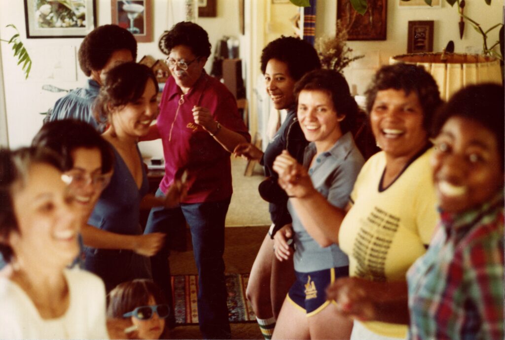 HIstoric color photo of ten women gathered indoors, smiling, and socializing together.