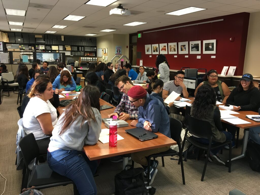 Students seated at multiple tables in the CSRC Library with papers, notebooks, and other materials.