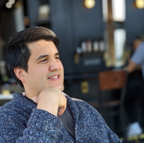 Emilio Cárdenas smiling with his hand under his chin indoors, against a blurred background.