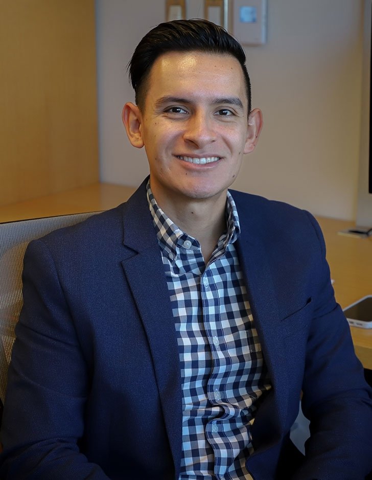 Cesar Vargas Nunez smiling in a navy blazer and checkered shirt and sitting in an office.