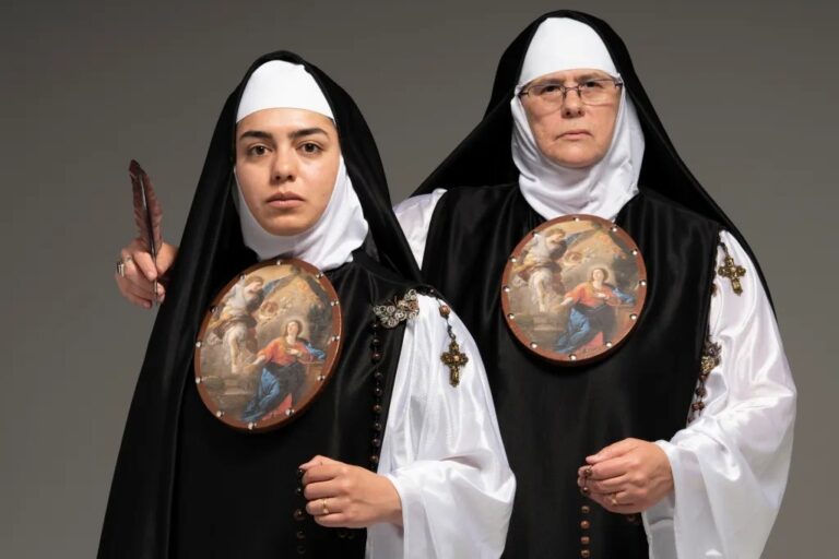 Art photograph of two women dressed as nuns standing side by side while holding a round religious image.
