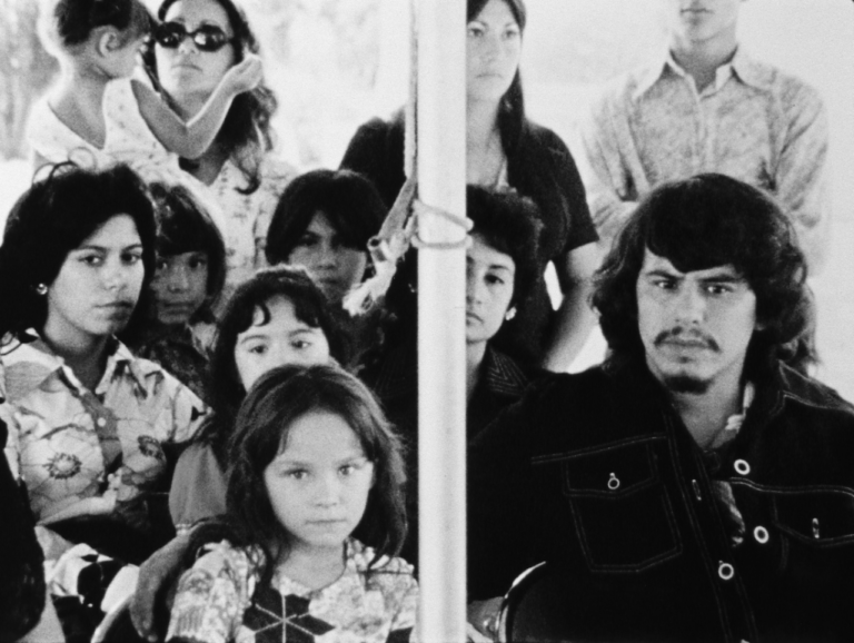 Black and white film still showing eleven people, including the filmmaker/star, adults and children, gathered closely together and facing the camera.