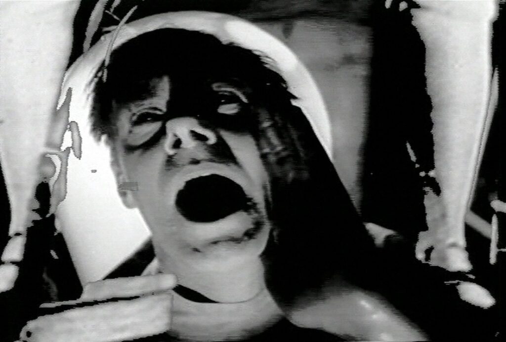 Black and white film still of a man laying down with his mouth opened.
