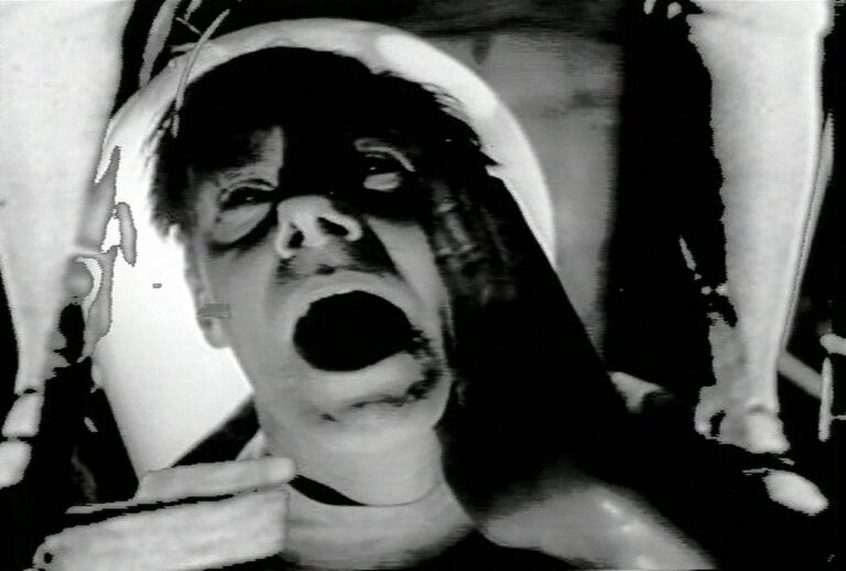 Black and white film still of a man laying down with his mouth opened.