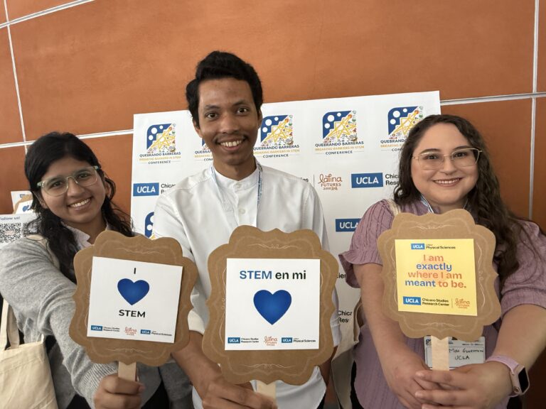 Three people smiling and holding STEM signs at a UCLA conference. Behind them is a backdrop with CSRC, Latina Futures, and conference logos.