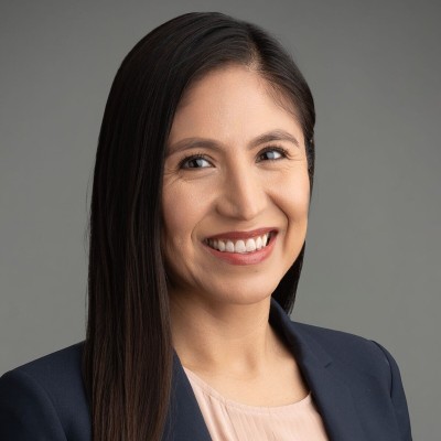 Professional headshot of a woman smiling with long dark hair wearing a black blazer.